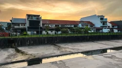 Two-storey terraced houses and a modern three-storey house along a riverbank at sunset