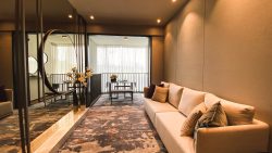 Living room with beige sofa, wall mirror, floral vases, and dining area near balcony with sheer curtains at Treasure At Tampines