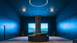 Architectural model of The Landmark tower in a dimly lit blue room with cityscape screens behind