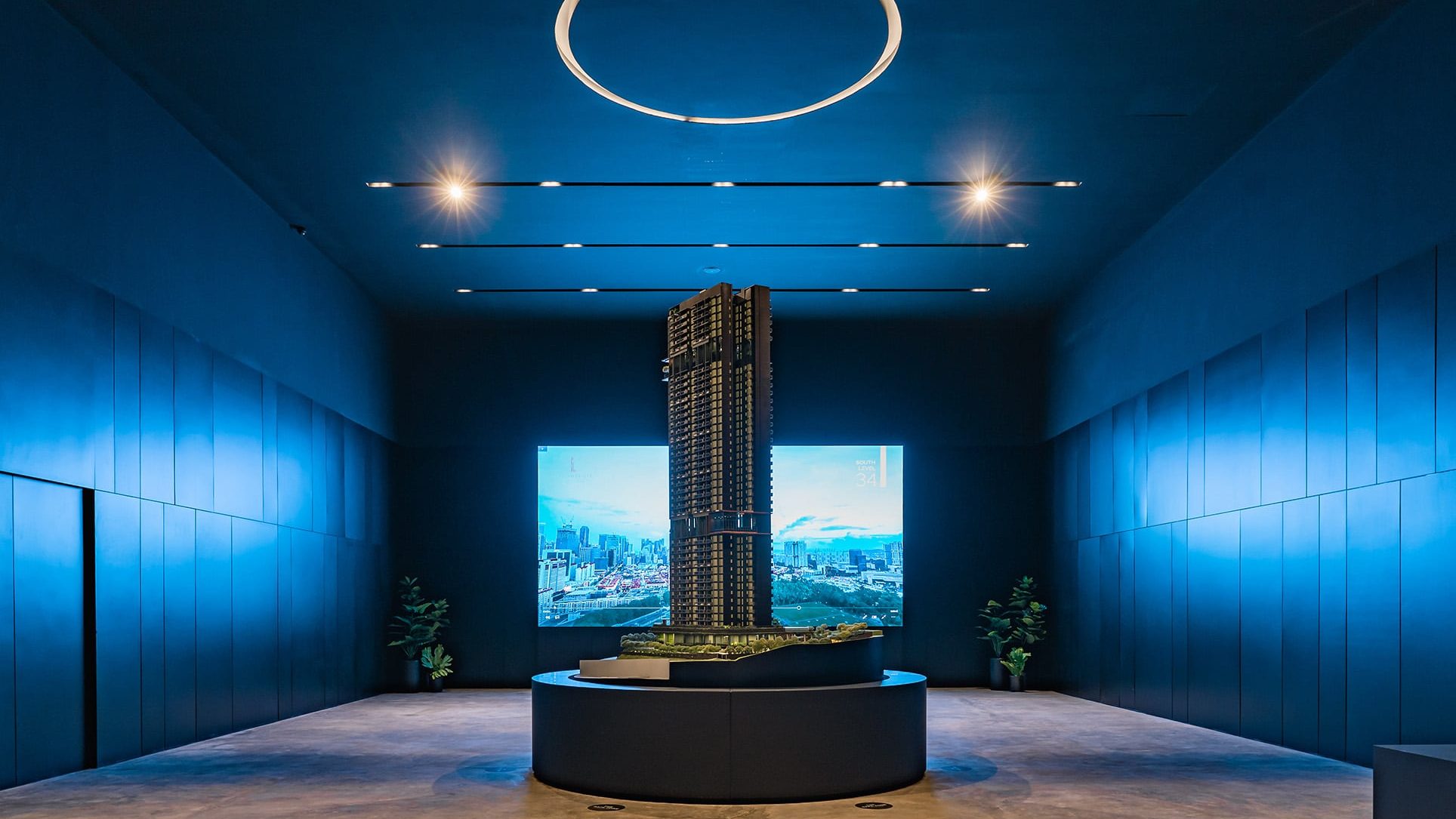 Architectural model of The Landmark tower in a dimly lit blue room with cityscape screens behind