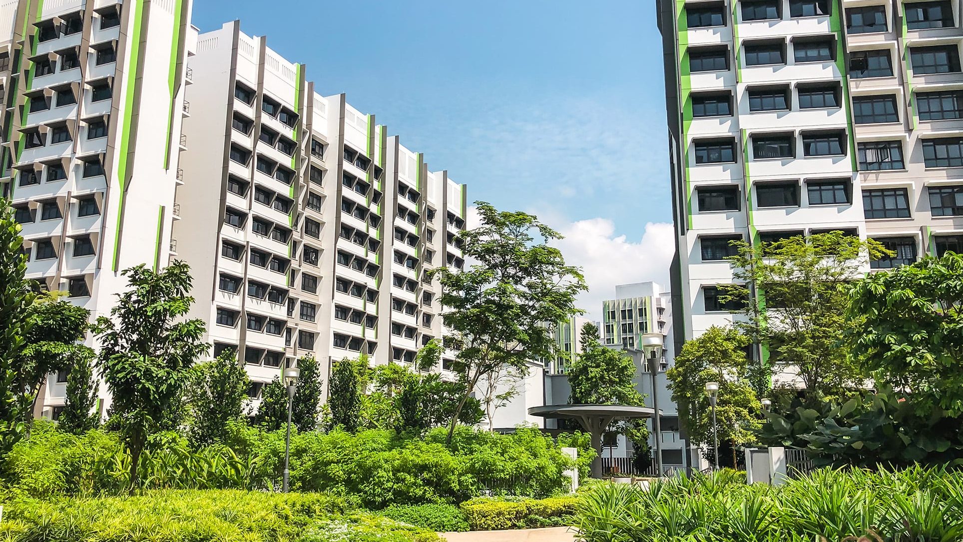 Alkaff Oasis residential blocks rising behind landscaped gardens with trees and shrubs under a clear blue sky