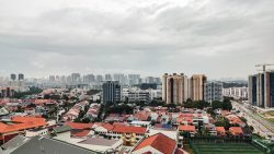Low-rise housing with red roofs in foreground and high-rise residential blocks with cranes under cloudy sky in background
