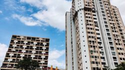 Two tall HDB blocks with beige and white facades under a partly cloudy sky
