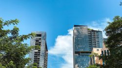 Two tall glass residential apartment blocks framed by trees under a blue sky with some clouds