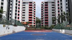 Outdoor basketball court with blue and red flooring in front of white and pink apartment blocks