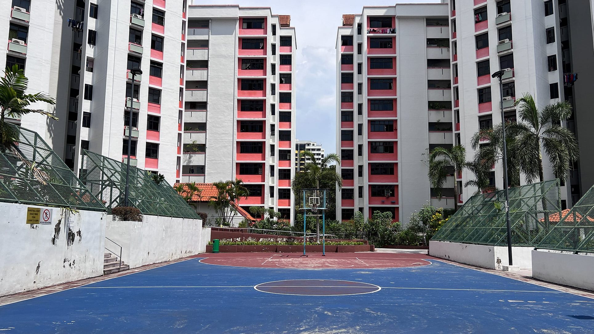 Outdoor basketball court with blue and red flooring in front of white and pink apartment blocks