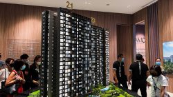 Amo Residence scale model with people wearing masks inside a sales gallery with wood panel walls