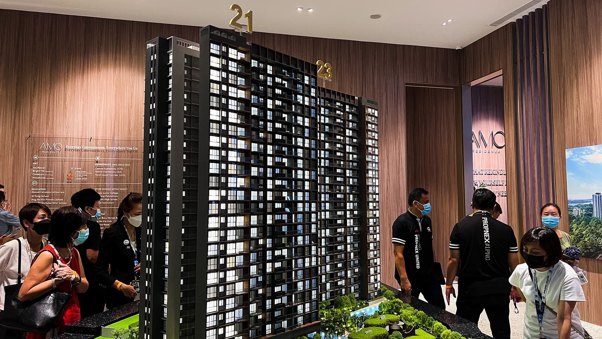 Amo Residence scale model with people wearing masks inside a sales gallery with wood panel walls