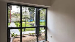 Window view from an empty room showing a garden with small trees, lawn, and hammocks outdoors