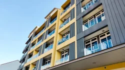 Yellow and grey apartment blocks with glass balconies against a clear blue sky