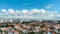 Low-rise landed terrace houses with orange roofs in foreground and tall apartments in background under blue sky