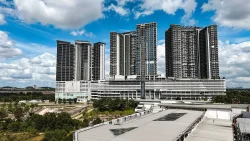 Tall residential blocks under partly cloudy sky with trees and roads in foreground