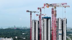 High-rise building structures under construction with multiple red and white tower cranes against a clear sky