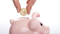 Hand holding a US dollar coin above a pink ceramic piggy bank with a coin slot