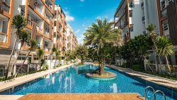 Outdoor swimming pool with palm trees and brown-framed apartment blocks on both sides at Parc Rosewood