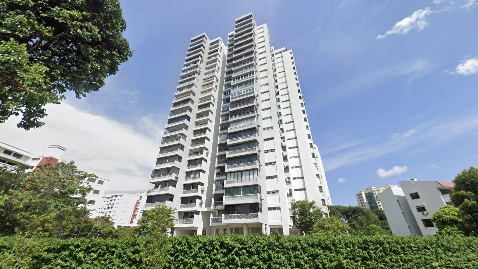 High-rise white residential apartment blocks surrounded by greenery and trees under a blue sky