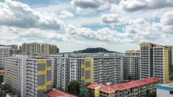 Housing blocks with yellow and grey accents under a partly cloudy sky with a small hill in the background