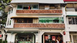 Two-storey building with brick balconies above a cafe with green awnings and a pedestrian walking past
