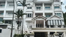 Large white multi-storey residential building with columns, balconies, a gate, and palm trees in front