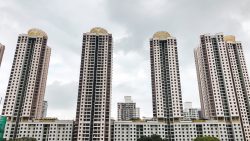 Four tall residential blocks with yellow lattice structures on roofs under a cloudy sky
