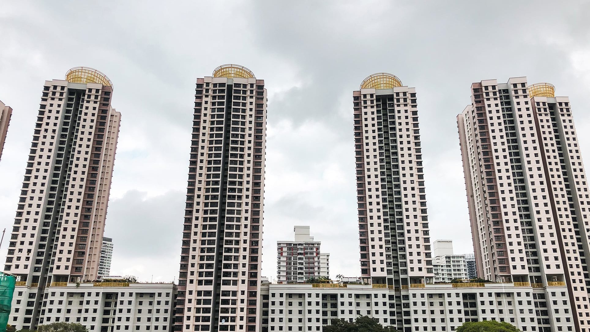 Four tall residential blocks with yellow lattice structures on roofs under a cloudy sky