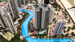 Architectural model of several tall residential and commercial buildings beside a blue canal and green areas