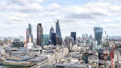 City skyline with tall modern office buildings and construction cranes under a partly cloudy sky