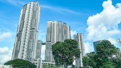 Tall residential apartment blocks with green trees and blue sky with clouds in the background