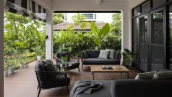 Covered terrace with black cushioned seats, wooden coffee table, and lush green plants outside