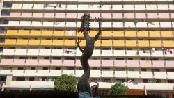Sculpture of a dragon in front of housing block with pastel-coloured balconies and laundry hanging