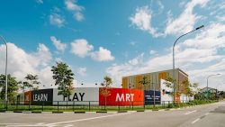 Construction site hoarding with words shop, dine, learn, play, MRT and childcare under a blue sky