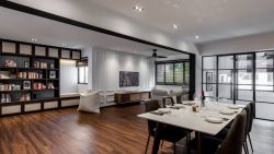 Open-plan living and dining area with wooden floors, built-in bookshelf, sofa, and dining table set for six people