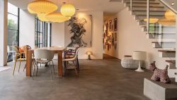 Dining area with mixed chairs, wooden table, hanging lantern lamps, staircase, and wall art in an open-plan interior