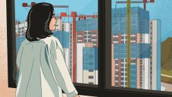 Woman in light jacket looking out window at construction site with cranes and high-rise buildings