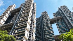 Tall residential apartment blocks with sky bridges against a blue sky and greenery at the base