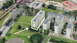 Tall residential blocks with solar panels on roofs near an open field and roads, one block outlined with arrow pointing