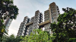 High-rise residential blocks with sky bridges framed by green trees under a cloudy sky