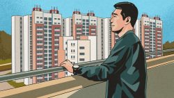 Man wearing a smartwatch looking out from a balcony at several high-rise housing blocks with blue sky background