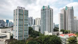 Housing blocks with green and yellow accents among trees and low-rise buildings under cloudy sky