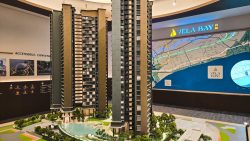 Scale model of Vela Bay residential blocks with pool and landscaped grounds, located in a showroom with a map display on the wall