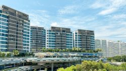 Watertown apartment blocks with blue-tinted windows behind Waterway Point mall and greenery under a blue sky