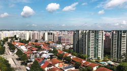 High-rise residential blocks beside low-rise houses with orange roofs along a tree-lined road under blue sky with clouds