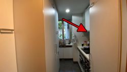 Narrow kitchen with white cabinets, black countertops, and a window overlooking greenery