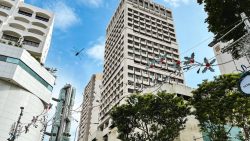 Taller commercial and residential blocks with Christmas decorations and trees below under a blue sky