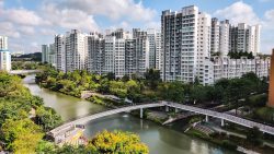 Waterway Woodcress residential blocks beside a river with a pedestrian bridge and greenery under a blue sky