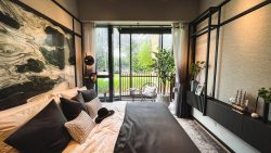 Bedroom with large bed, black and white cushions, abstract wall art, and balcony with chairs and plants