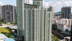Tall residential blocks with green and white facades near a road and MRT tracks on a sunny day
