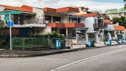 Two-storey terrace houses with orange-tiled balconies along a roadside corner with street signs and bins
