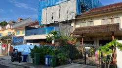 Terraced houses with some under construction, greenery, waste bins, and motorcycles on the street in front