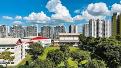 Sengkang Secondary School buildings and green field with high-rise housing blocks under blue sky and clouds